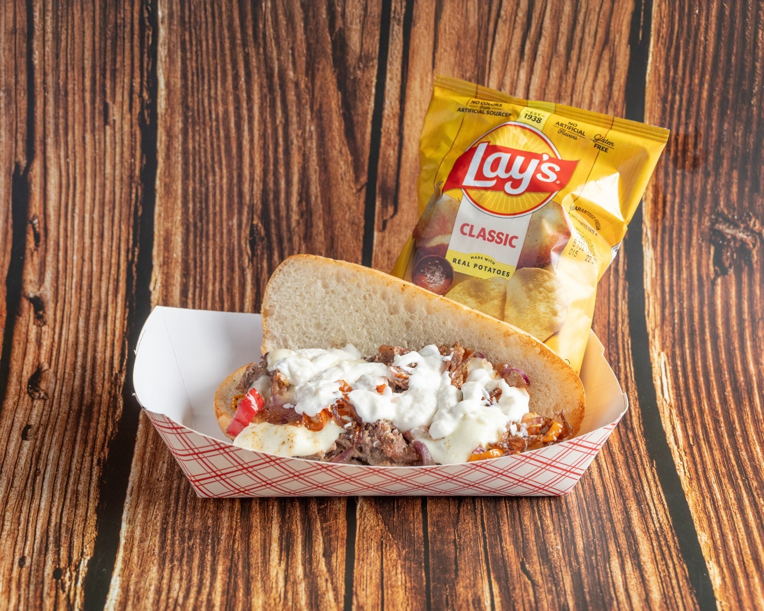 A filled sandwich topped with creamy sauce, served with chips